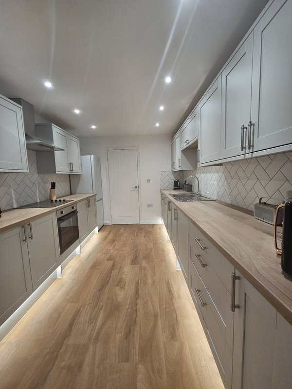 Modern galley kitchen with white cabinetry, wood-effect countertops and herringbone backtile.