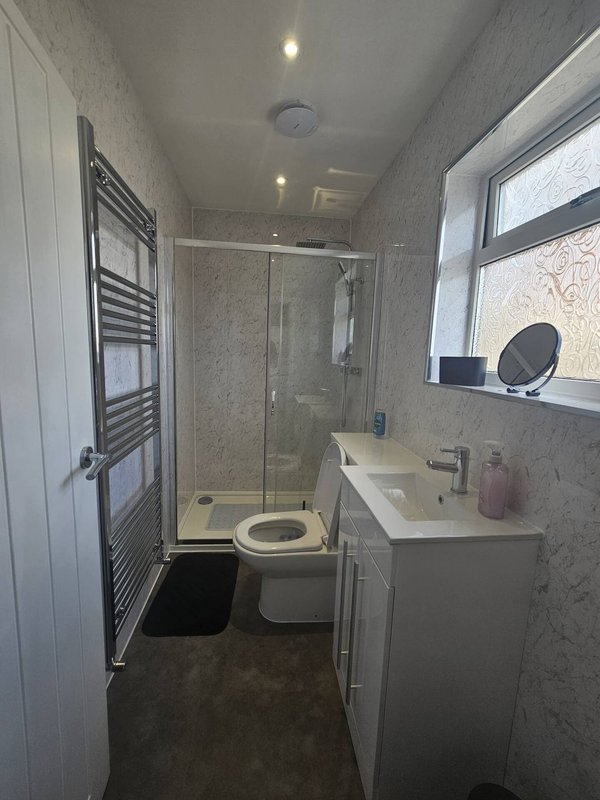 Modern bathroom with shower enclosure, toilet, sink, heated towel rail and window