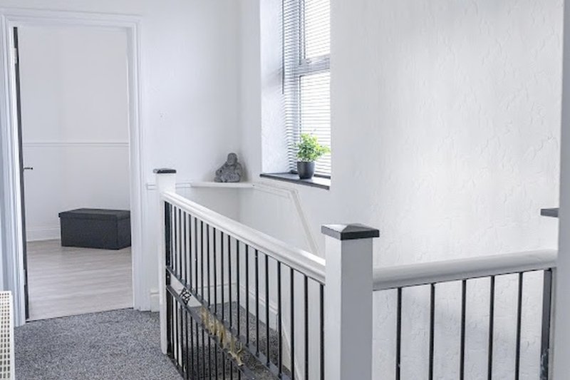 Modern staircase landing with white walls, metal railings, window and gray carpet