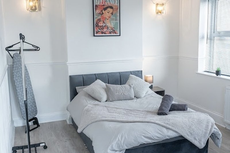 Modern bedroom with double bed, grey headboard, white bedding, and decorative wall art