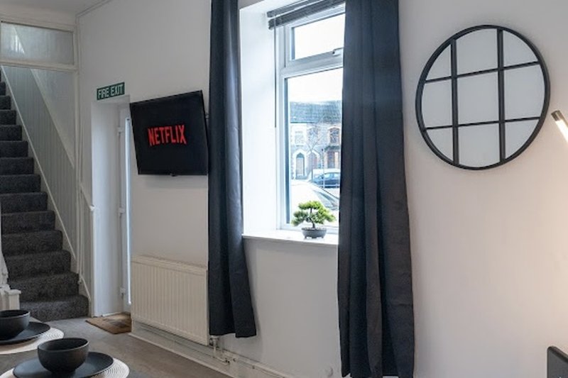 Modern living room with wall-mounted TV, large window with dark curtains, circular mirror and staircase