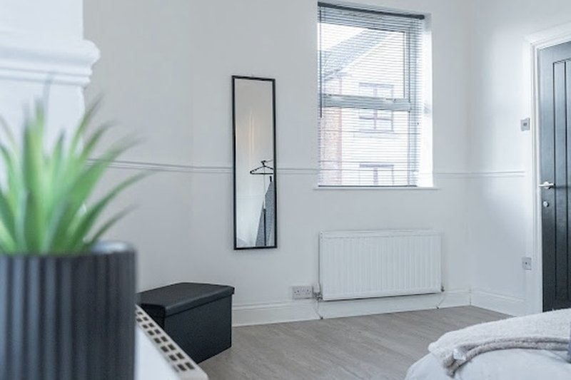 Bright modern bedroom with wooden floor, radiator, mirror, window and potted plant