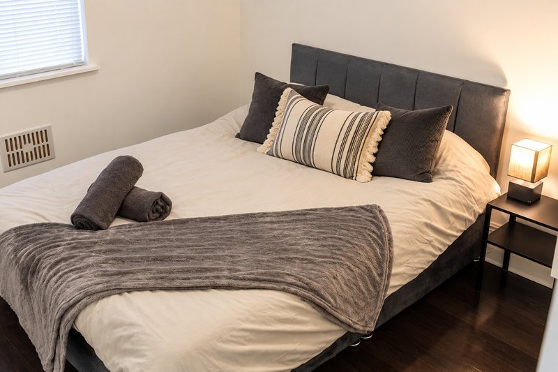 Bedroom with queen bed, dark headboard, striped pillows, folded blanket, and bedside lamp