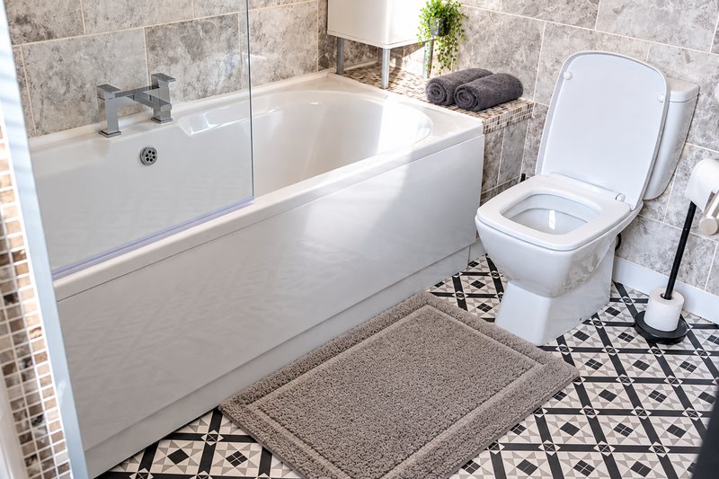 Modern bathroom with white bathtub, toilet, shower enclosure, and geometric tile flooring