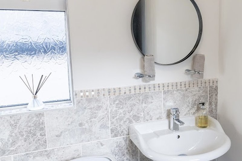 Modern bathroom with white sink, round mirror, marble tile backsplash and window