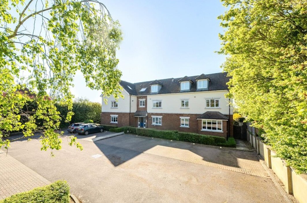 Modern brick and white apartment building with driveway, parked cars and mature trees surrounding