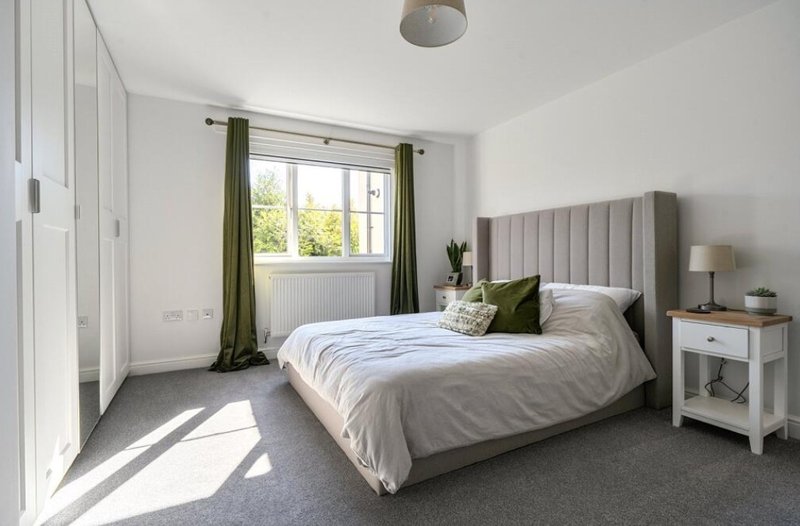 Bright bedroom with double bed, grey upholstered headboard, olive curtains and white furniture