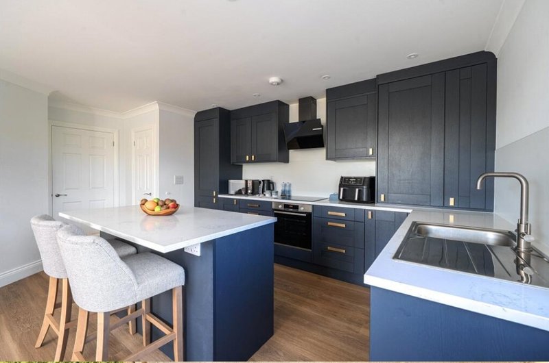 Modern kitchen with dark blue cabinetry, white countertops, island seating and wooden flooring