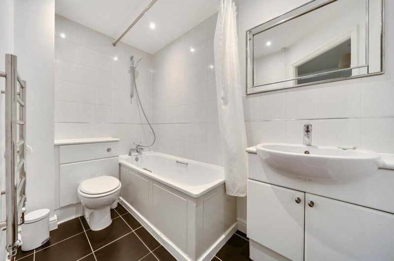 Modern bathroom with white subway tiles, bathtub, toilet, curved sink and mirror