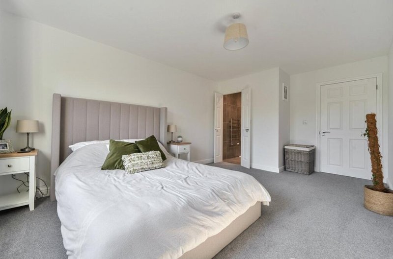 Spacious bedroom with upholstered headboard, white bedding, grey carpet and ensuite door