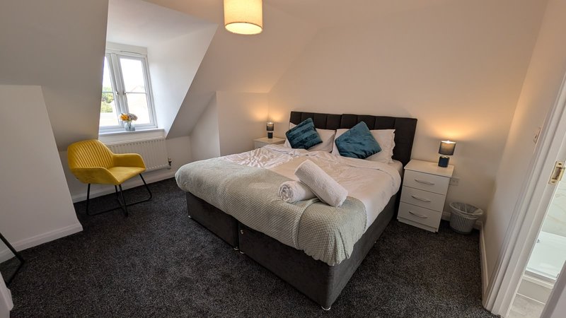 Attic bedroom with double bed, yellow armchair, bedside tables and sloped ceiling
