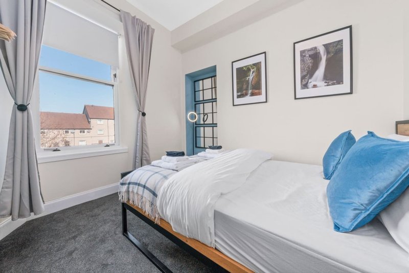 Bright bedroom with double bed, blue pillows, window with city view, framed wall art
