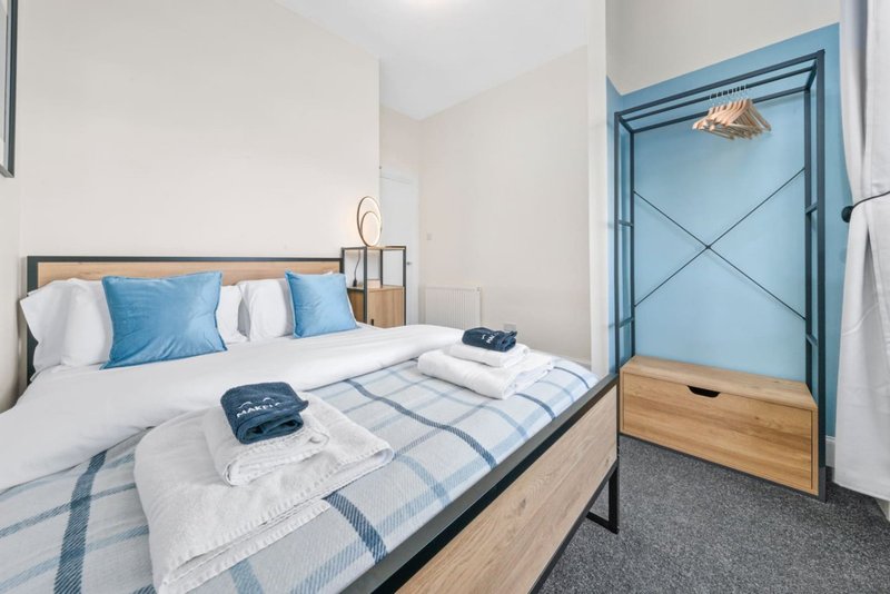 Modern bedroom with double bed, blue pillows, wooden frame and blue wardrobe door