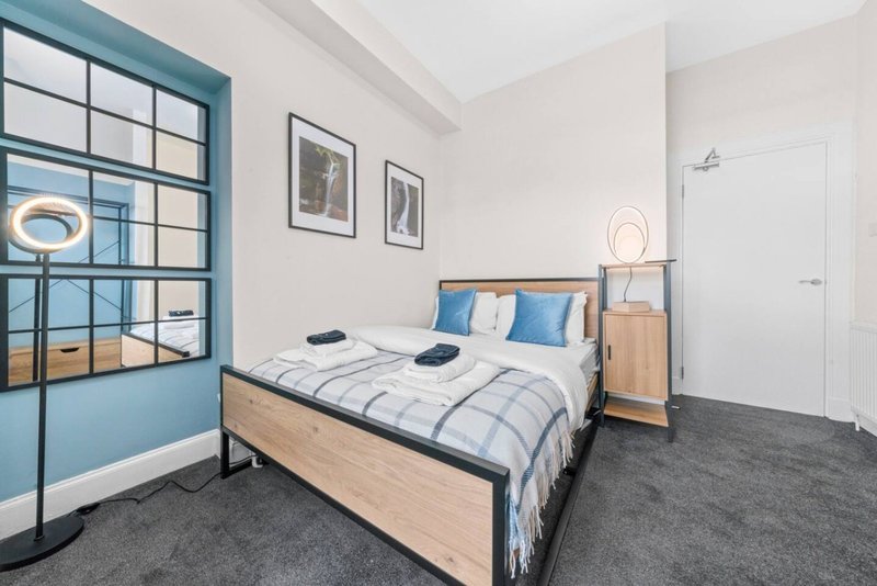 Modern bedroom with double bed, wooden frame, blue headboard cushions, and teal-framed window