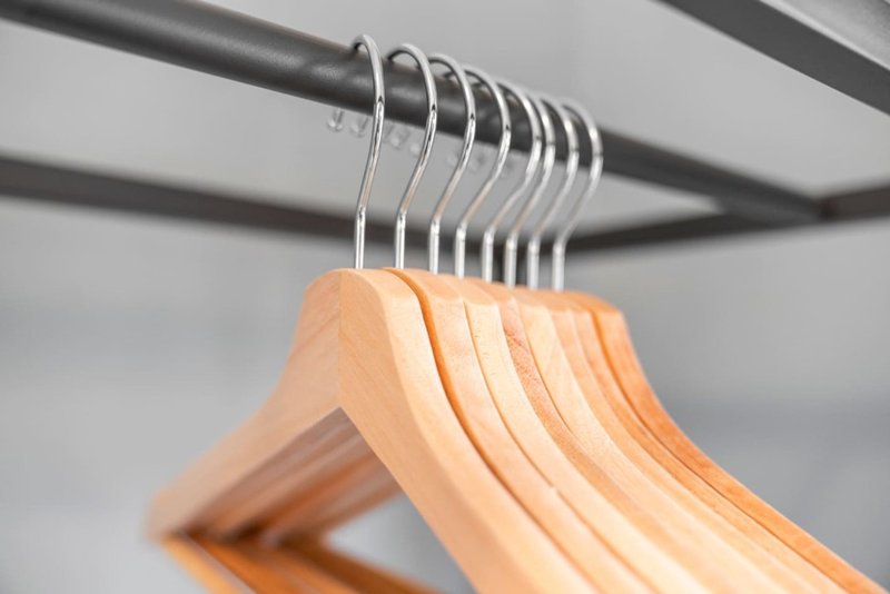 Row of wooden coat hangers hung on metal rail against white ceiling
