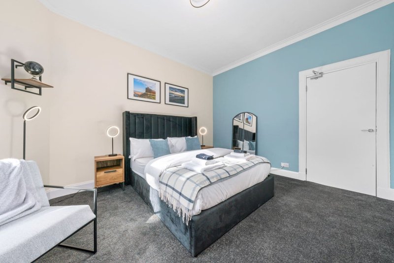Modern bedroom with double bed, blue accent wall, wooden nightstand and grey carpet flooring