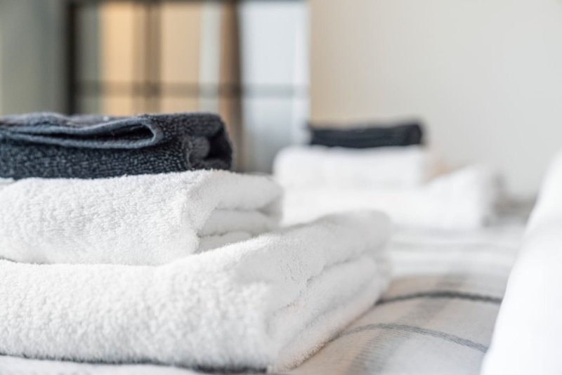 Folded towels in white and dark colors arranged on bed with window in background