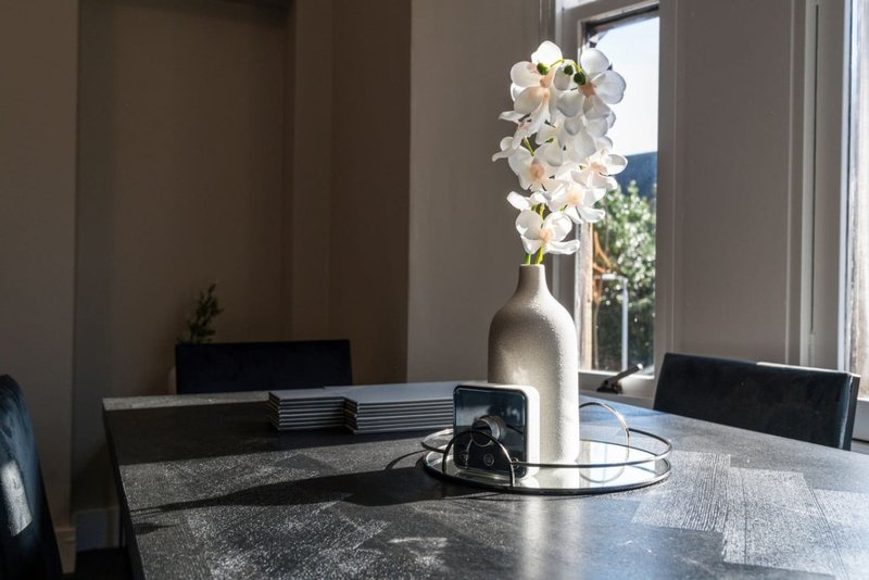 Modern dining table with white orchid arrangement, black chairs, and natural light from window
