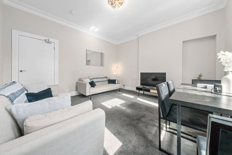 Modern living room with light grey sofas, black TV stand, desk area, and neutral decor