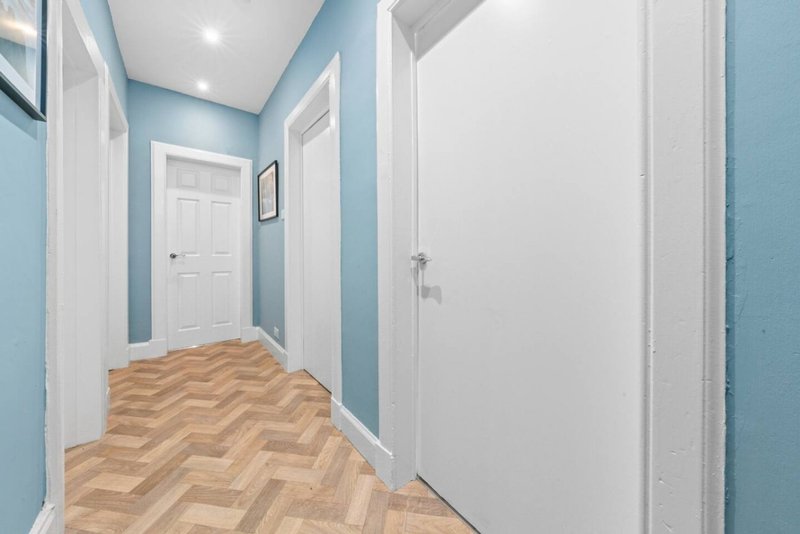 Light blue hallway with herringbone wood flooring, white doors and trim
