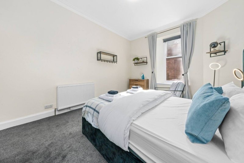 Bright bedroom with two single beds, white bedding, blue throw, and window with grey curtains