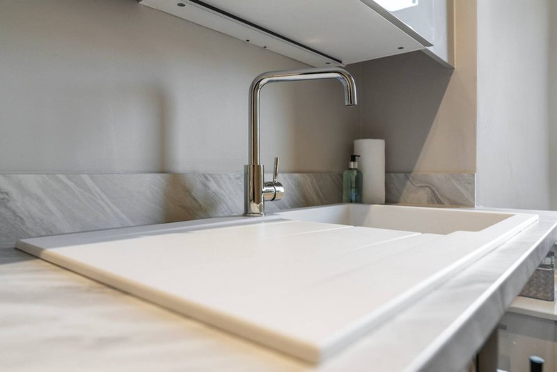 Modern kitchen sink with marble backsplash, chrome faucet and white countertop