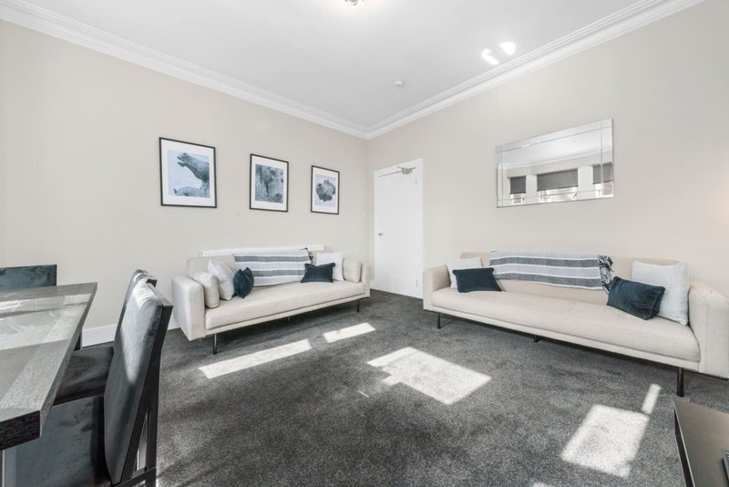 Open-plan living area with two cream sofas, grey carpet, dining table, and framed artwork on walls