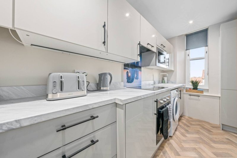 Modern white kitchen with marble countertop, appliances, and wooden herringbone flooring
