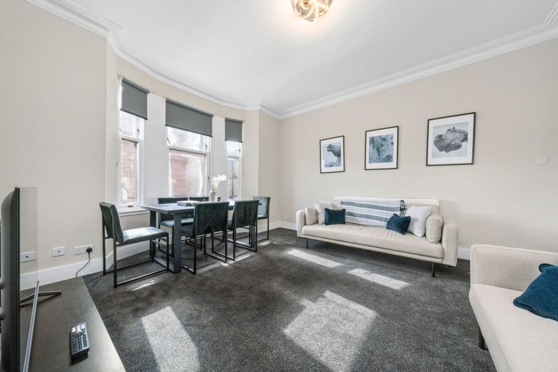 Bright living room with dining table, sofa, large windows and framed wall art