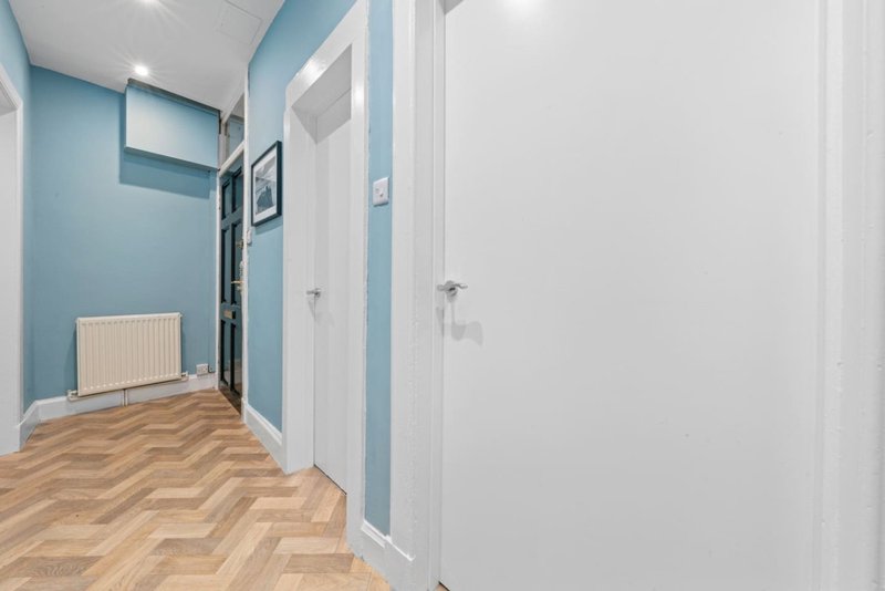 Bright hallway with blue walls, herringbone wood flooring, white doors and radiator
