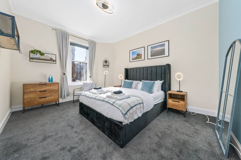 Bright modern bedroom with king bed, wooden dresser, grey carpet, and garden view