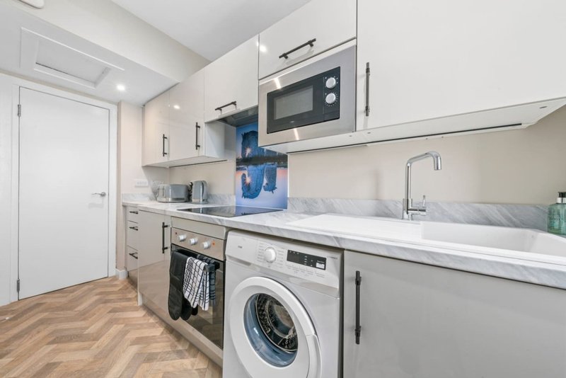 Modern kitchen with white cabinets, stainless steel appliances, washing machine and wooden floor