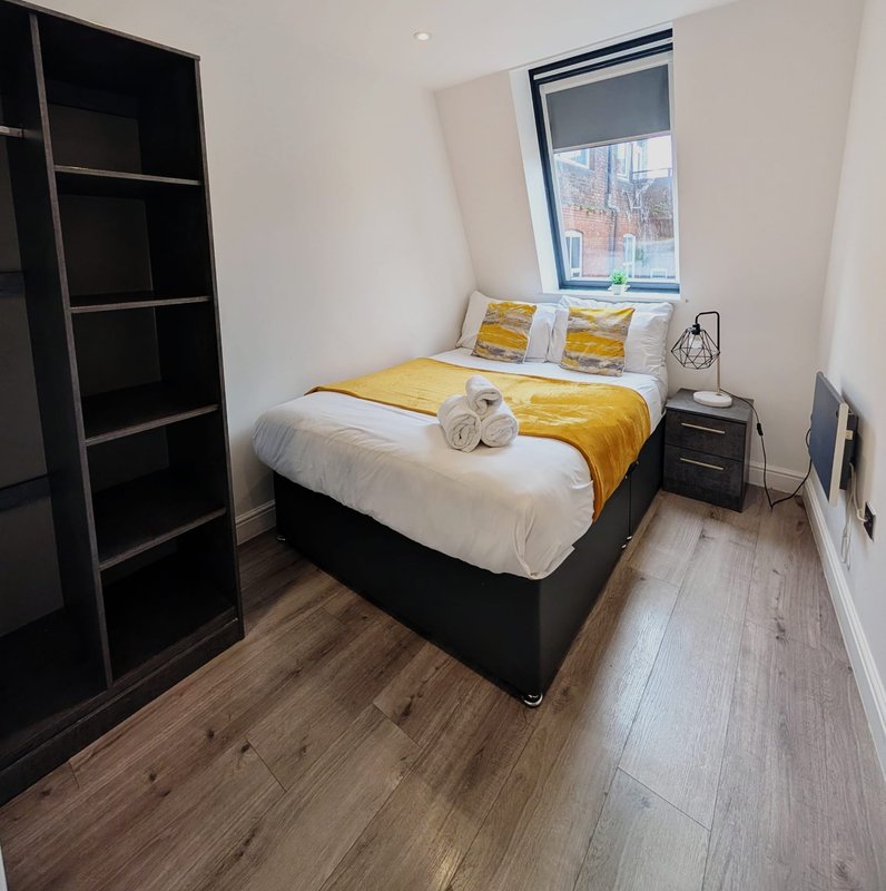 Modern bedroom with double bed, yellow bedding, black shelving unit and wooden floor