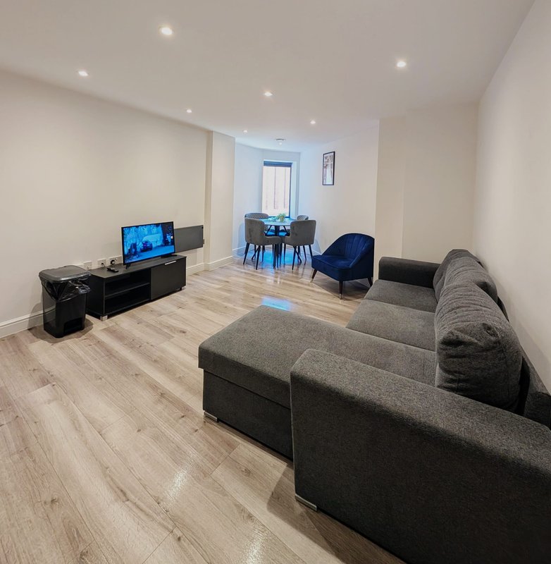 Open-plan living room with grey sofas, TV, wooden flooring, and dining area visible