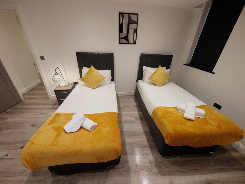 Twin bedroom with two single beds, yellow cushions and throws, black headboards