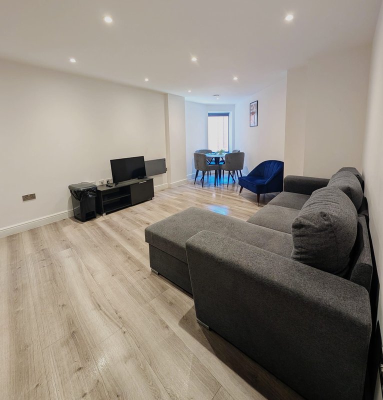 Modern living room with gray sofas, TV, dining area with blue chairs, wooden flooring