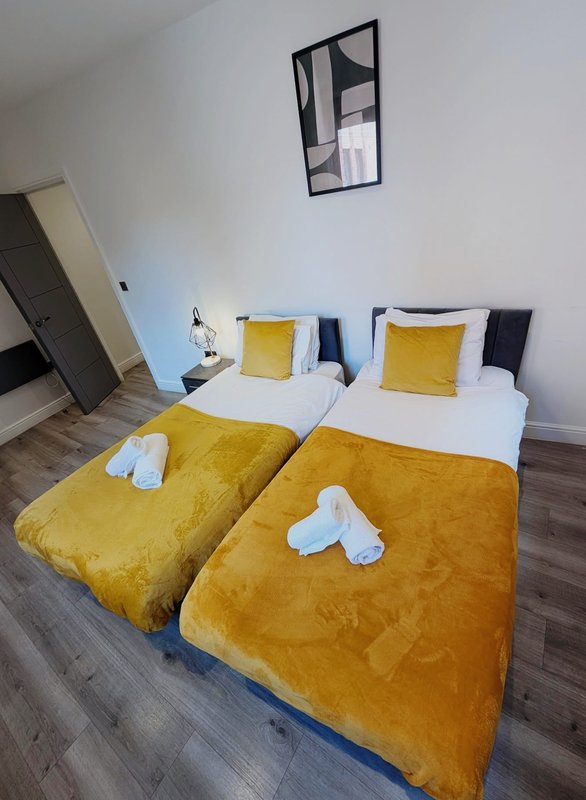 Twin beds with yellow quilts and cushions, white pillows, wooden floor, wall art
