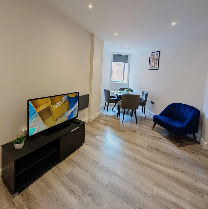 Modern living room with TV, dining table and blue armchair, wooden flooring