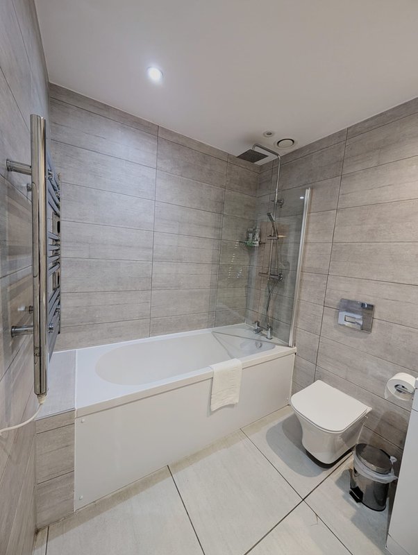 Modern bathroom with bathtub, shower enclosure, toilet, heated towel rail and tiled walls