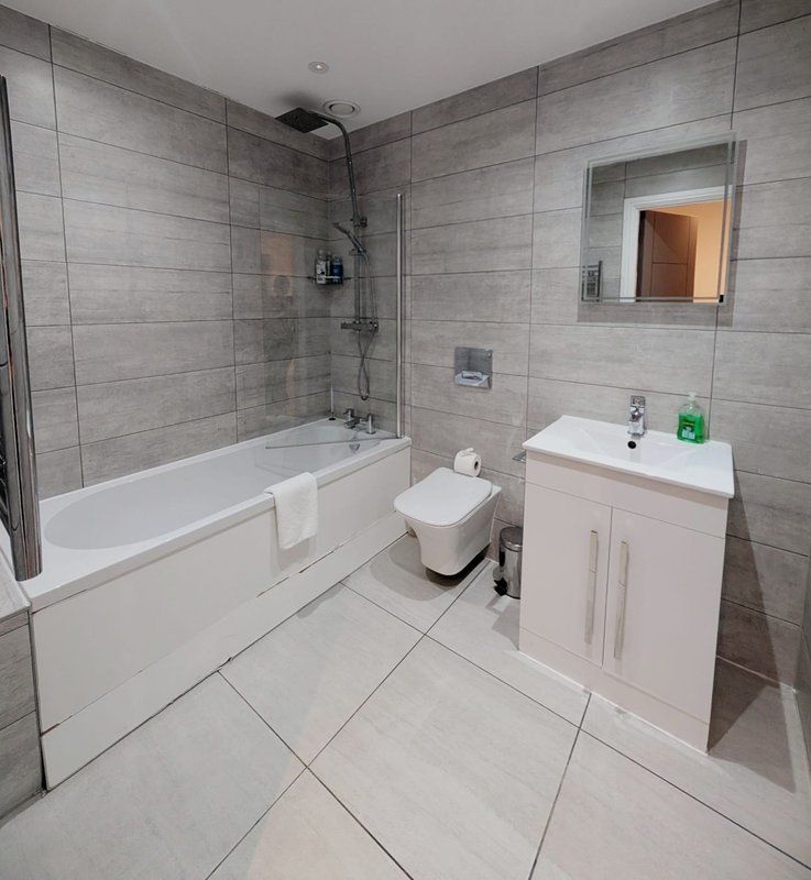 Modern bathroom with bathtub, toilet, white vanity sink and grey tile walls