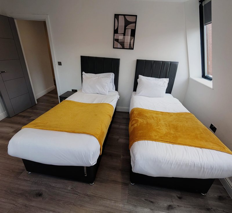 Twin bedroom with two single beds, yellow throws, white pillows, wooden flooring