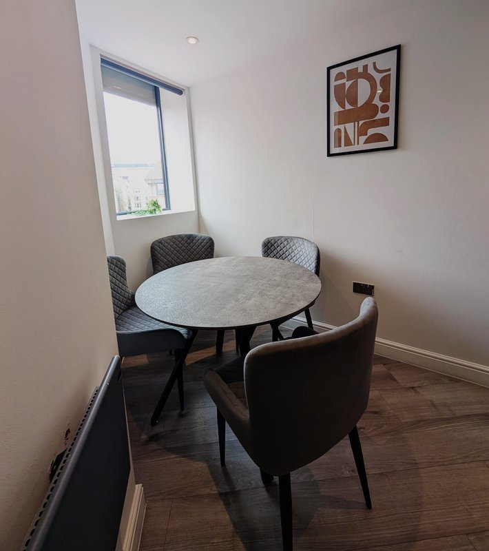 Modern dining area with round marble table, three grey upholstered chairs, window view, and framed wall art