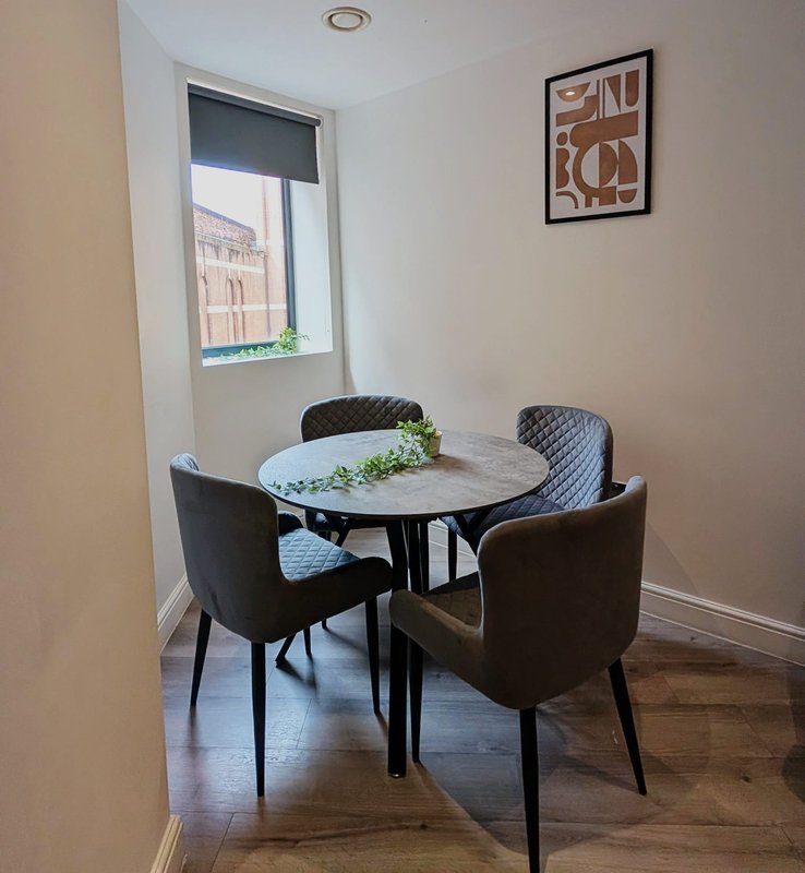 Dining area with round marble table, four upholstered chairs, window with city view, and framed wall art