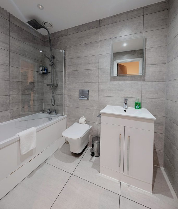 Modern bathroom with grey tile walls, white vanity, bathtub with glass shower enclosure and mirror