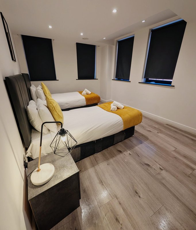 Modern bedroom with two beds, yellow bedding accents, wooden flooring and wall-mounted lights