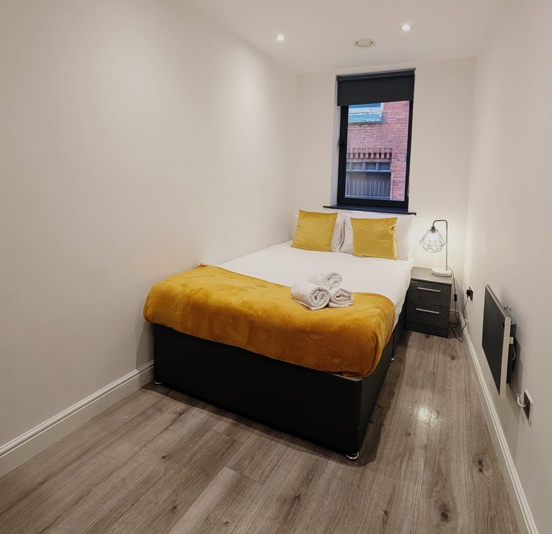 Compact bedroom with double bed, yellow bedding, small window, and wooden flooring