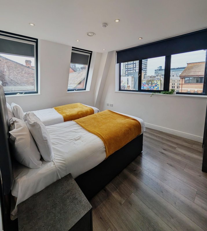 Modern bedroom with double bed, yellow throw, white bedding, dark wood flooring and windows