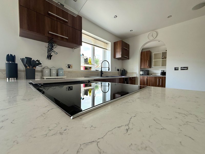 Modern kitchen with marble countertops, dark wood cabinets, and central island with hob