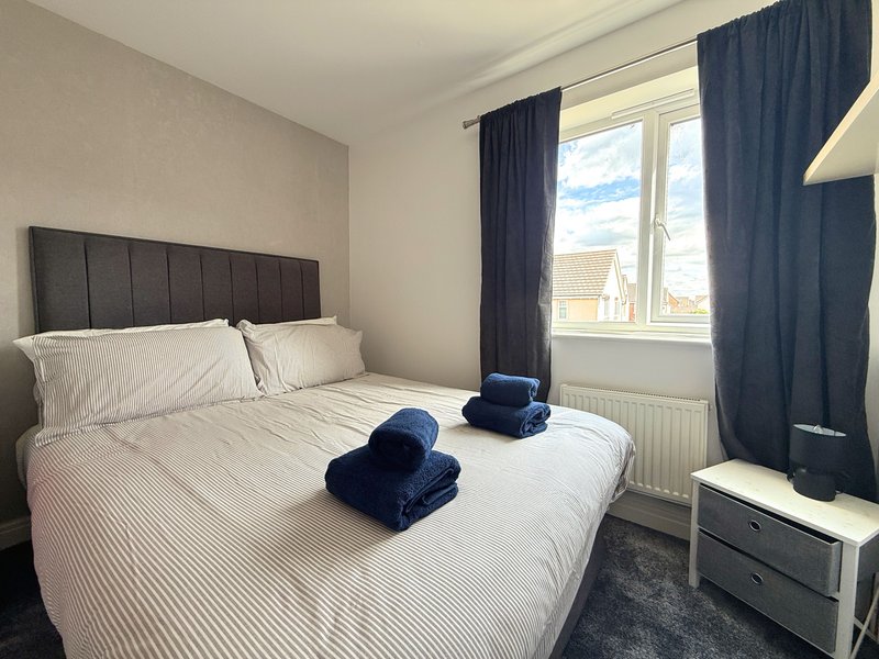 Bedroom with double bed, dark headboard, folded towels, window with blue curtains
