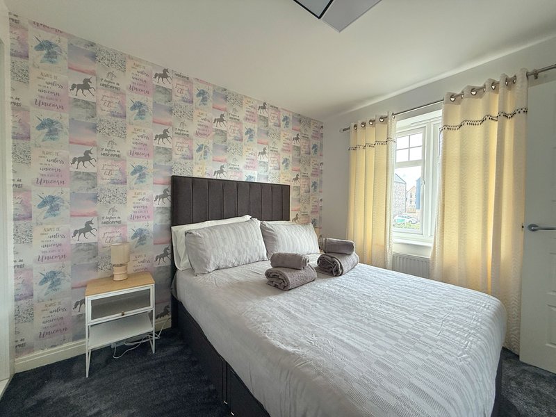 Bedroom with double bed, patterned wallpaper, bedside table, and yellow curtains